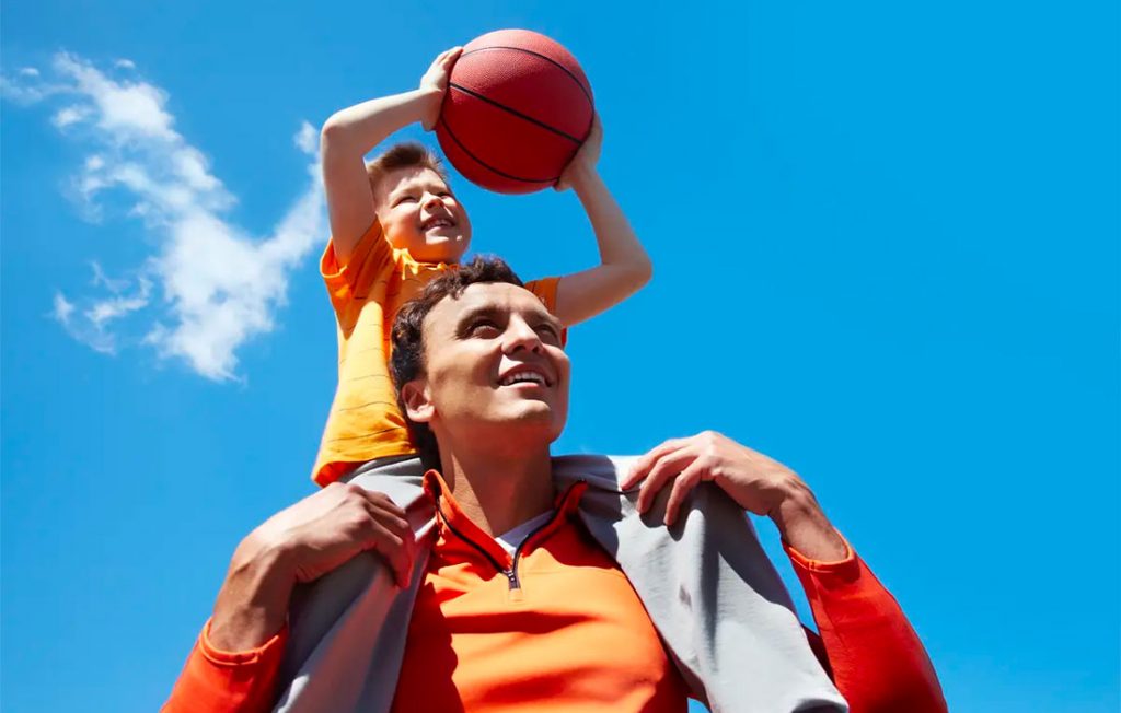 parent and son together outside, son on dad's shoulders and holding a basketball
