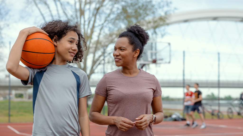 African American Mother and Her Teenage Son With a Ball on the Basketball Court Outdoors.