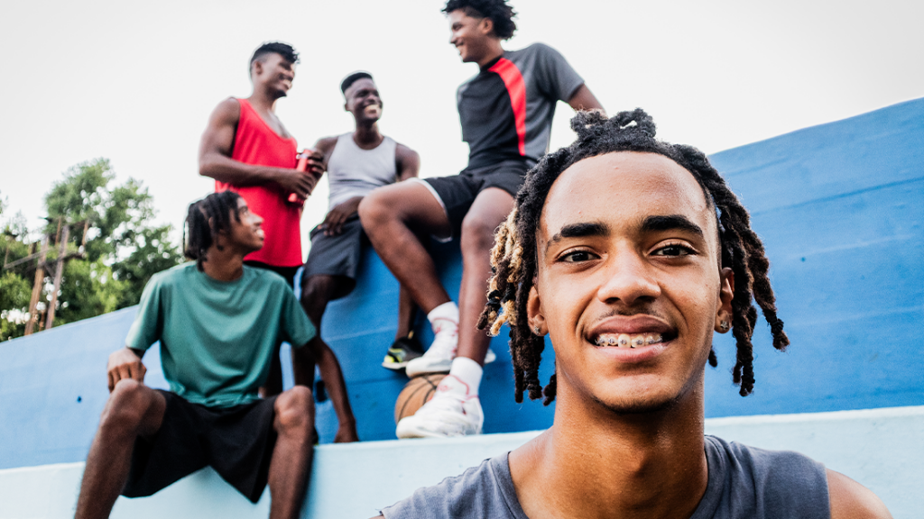 Portrait of a Gen Z basketball player, at on outdoor court and with teammates in the background.