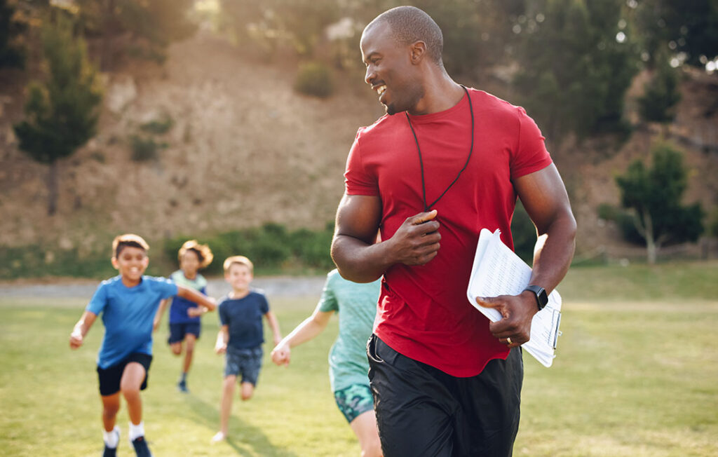 Coach with clipboard having a running session with group of kids.