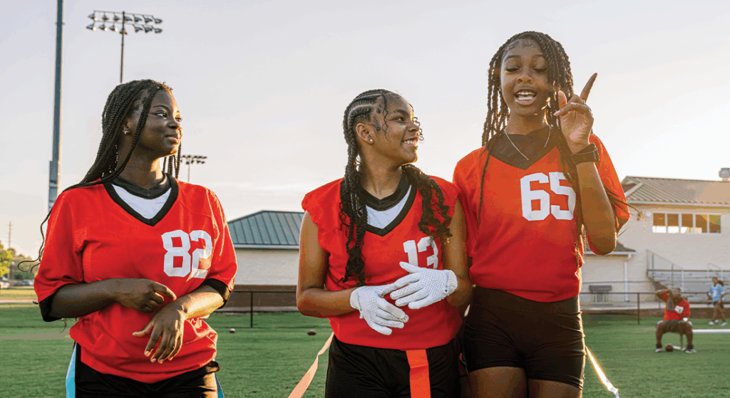 Three youth flag football players talking and practicing together.