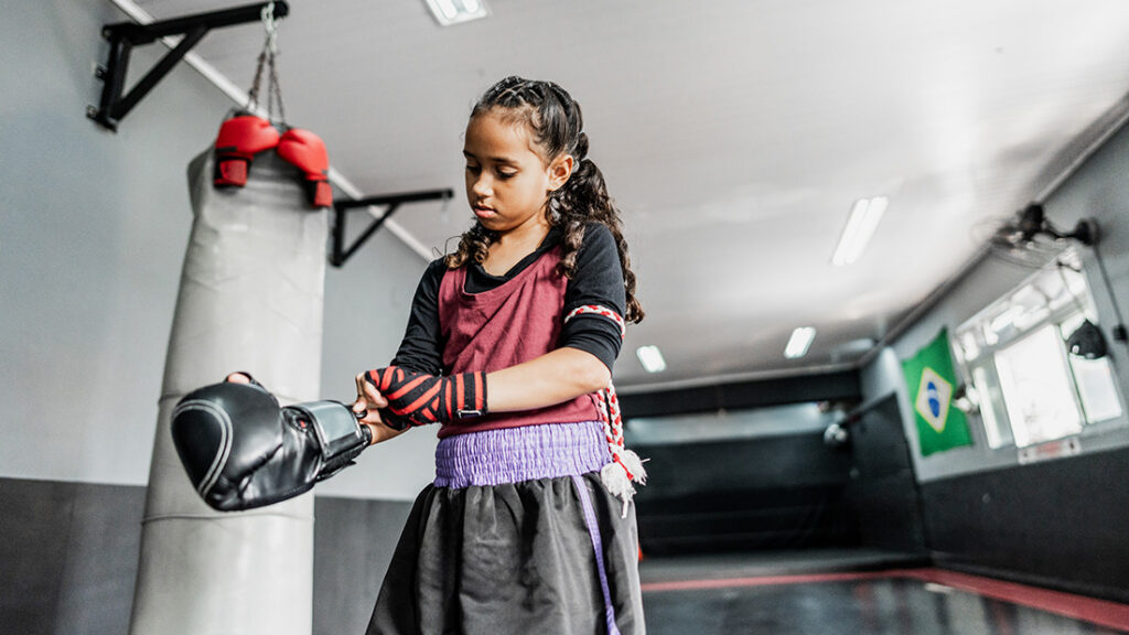 Young girl putting on boxing glove in a gym with a punching bag