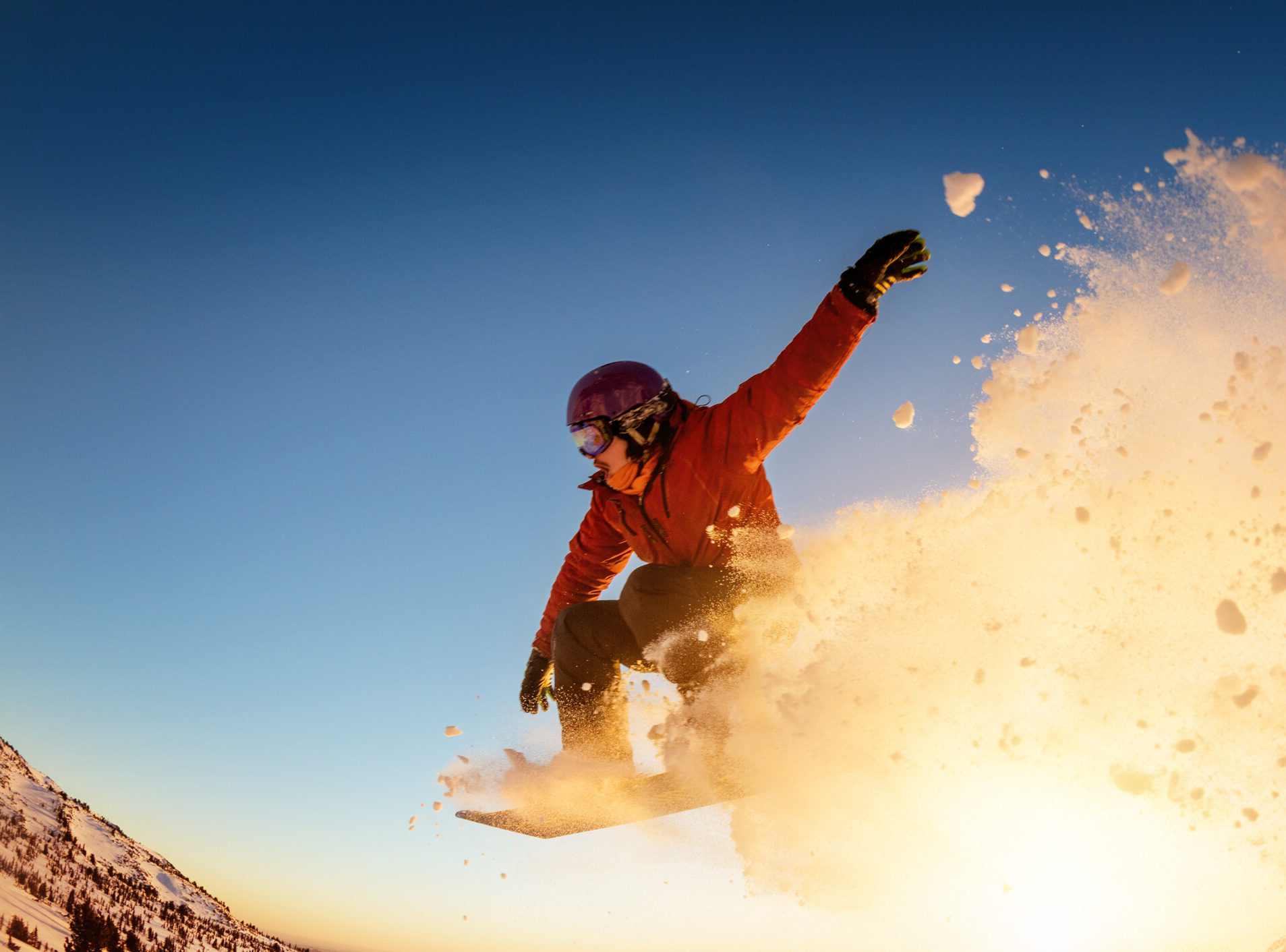 Snowboarder jumps or flies against sunset light with snow dust